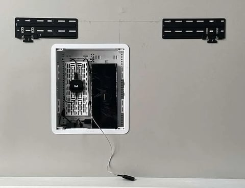 White recessed electrical outlet or device box installed in drywall with visible internal components and wiring, flanked by black mounting brackets