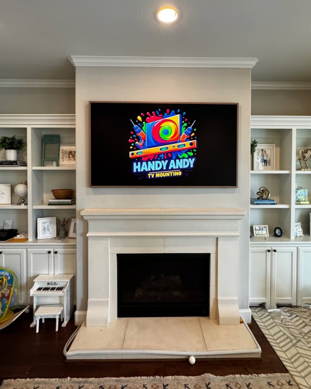 White fireplace with mounted TV displaying Handy Andy logo, flanked by built-in shelving in modern living room