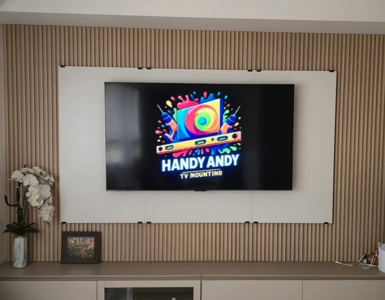 Flat-screen TV professionally wall-mounted on a wood-slat accent wall, displaying the Handy Andy TV Mounting logo