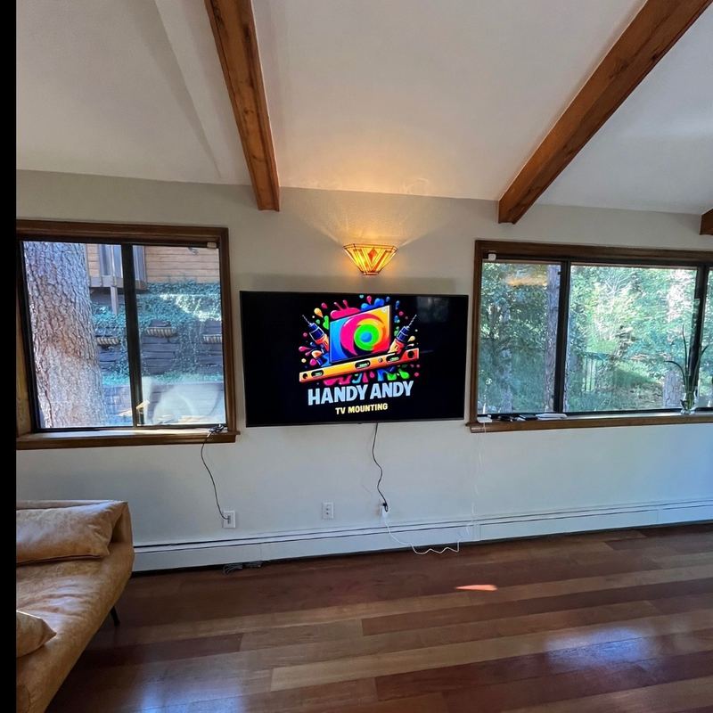 TV mounted on a living-room wall between two large windows, under exposed wood ceiling beams