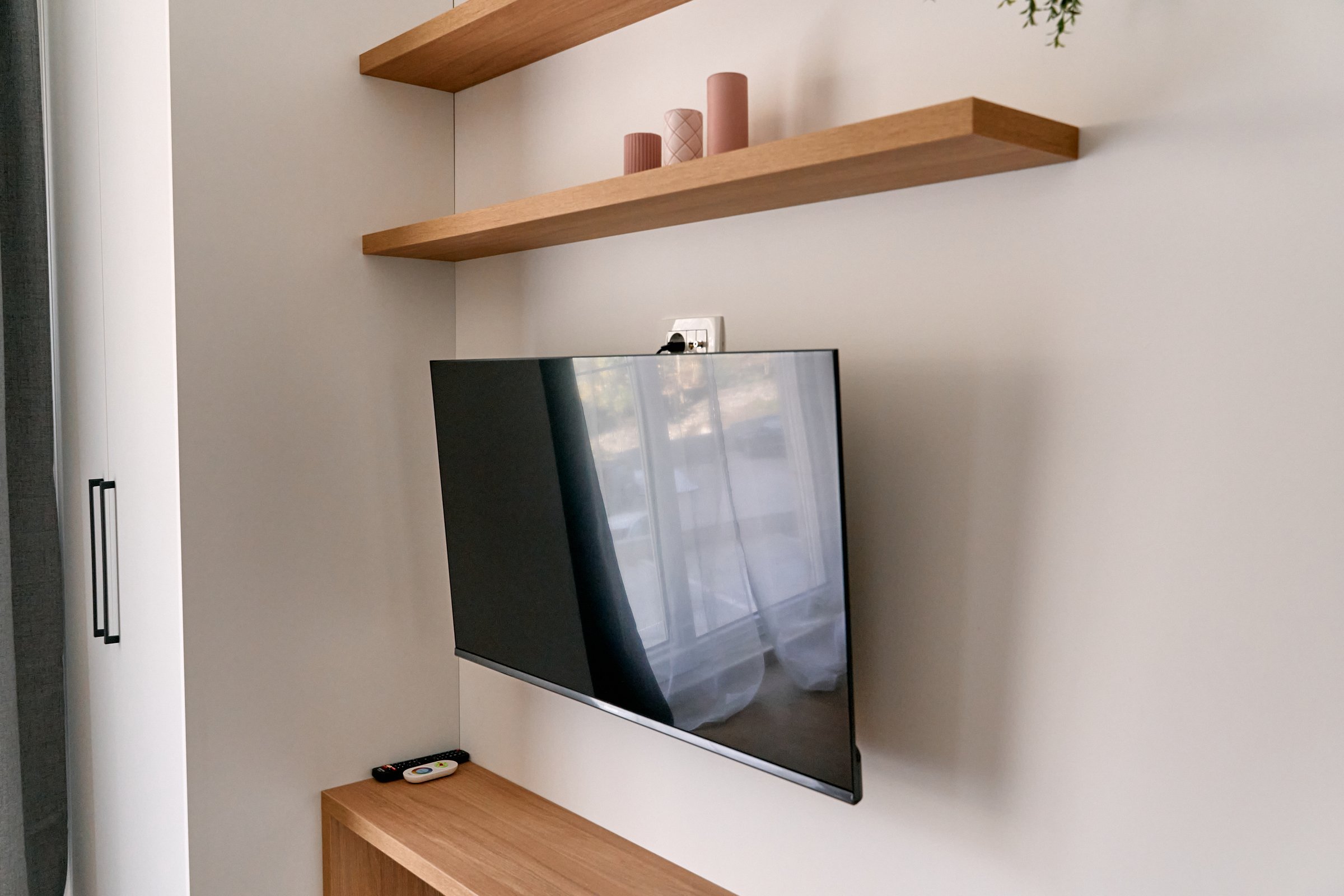 A modern living room features a wall-mounted tv and wooden shelves, exemplifying minimalist design and functionality for a sleek, contemporary aesthetic.
