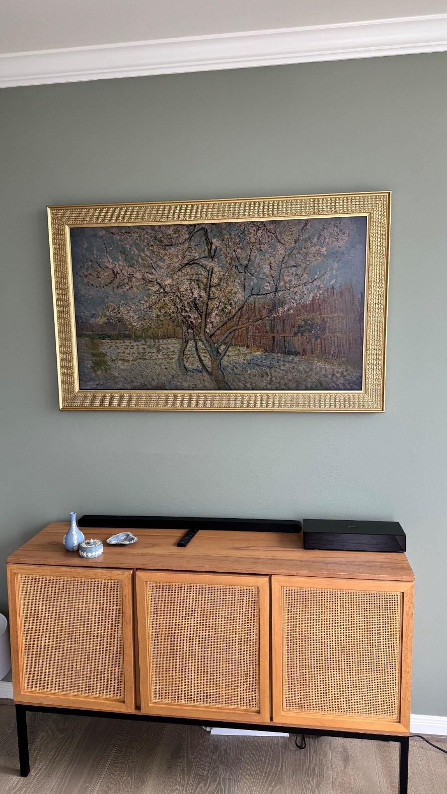 Samsung Frame TV with a custom gold bezel in art mode showing a Van Gogh painting, flush mounted on a sage green wall above a credenza