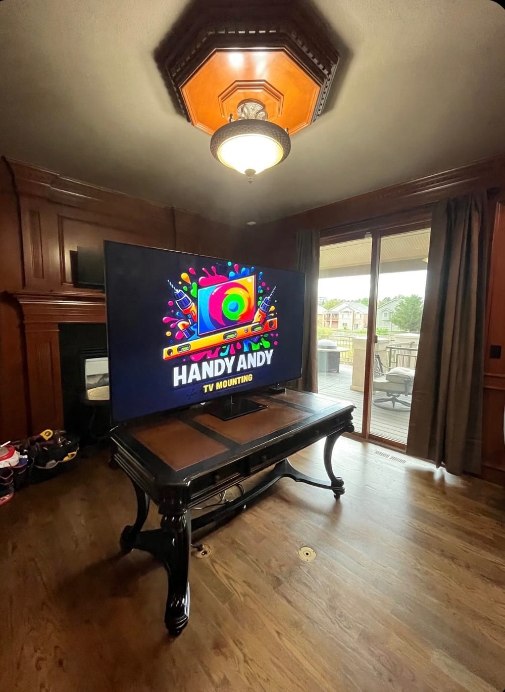 TV mounted on dark wood paneling in a room with an octagonal ceiling light, displaying the Handy Andy logo