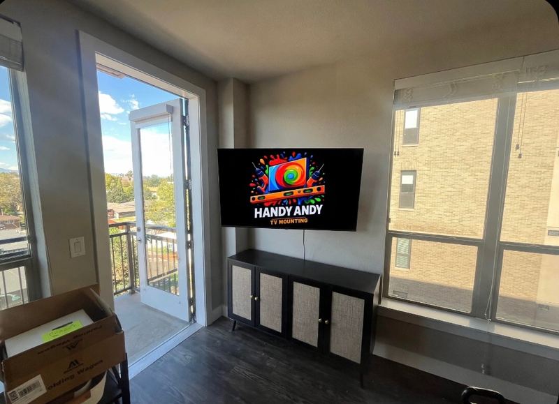 TV mounted above a black cabinet in an apartment living room, between an open balcony door and tall windows