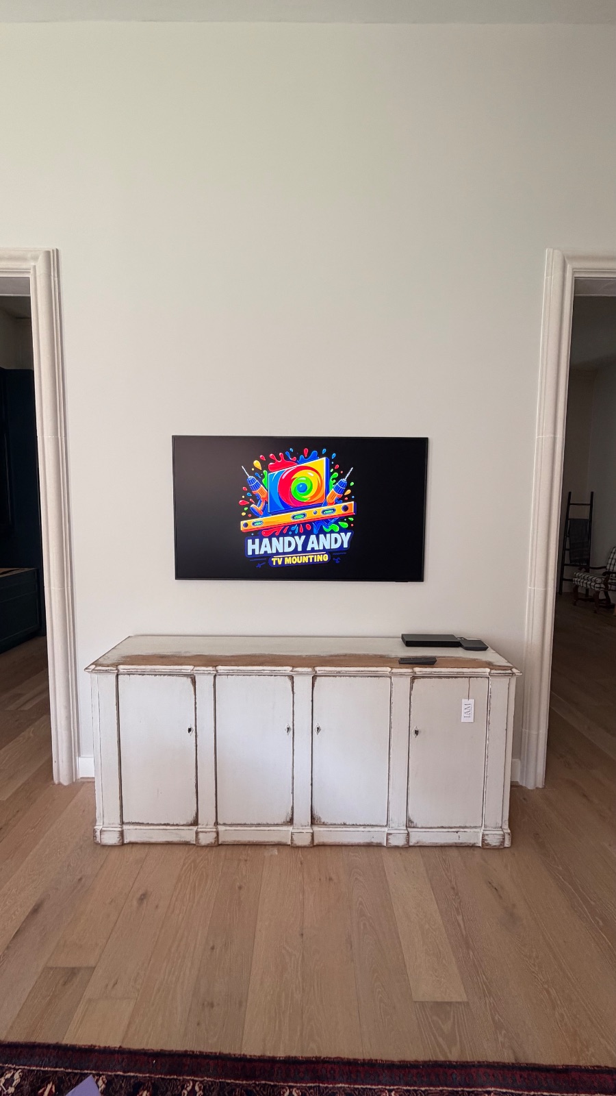 TV mounted above a distressed white console cabinet between two doorways displaying the Handy Andy logo