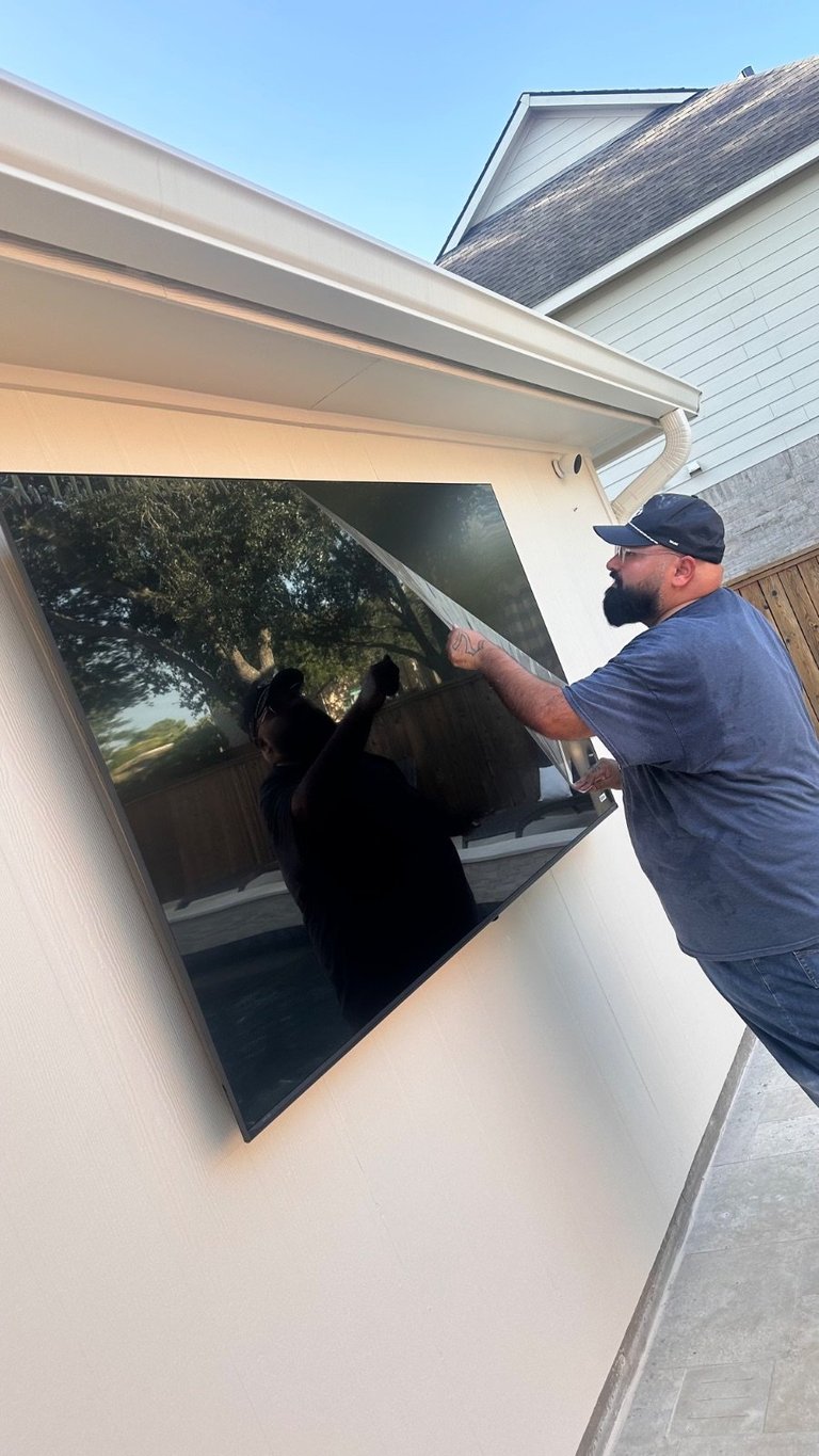 Man installing black solar shade screen on large residential window under white aluminum awning