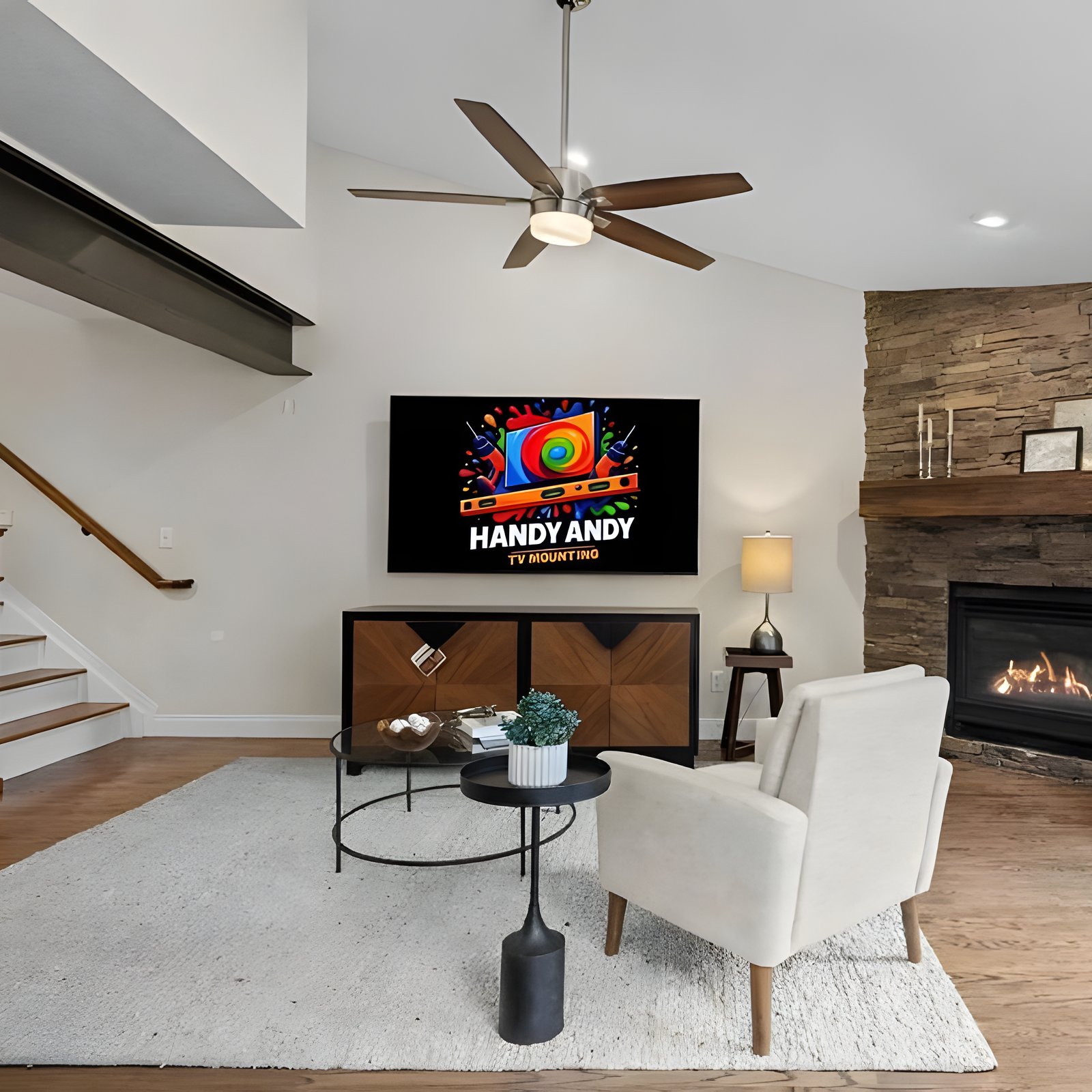 TV mounted above a wood media console in a living room with a stacked-stone corner fireplace, showing the Handy Andy logo