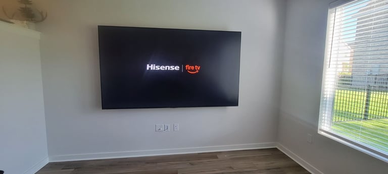 Hisense Roku TV mounted on white wall in empty room with wooden floor and large window