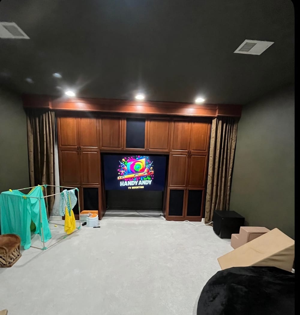 TV mounted in a dark wood built-in entertainment wall in a large carpeted room, displaying the Handy Andy logo