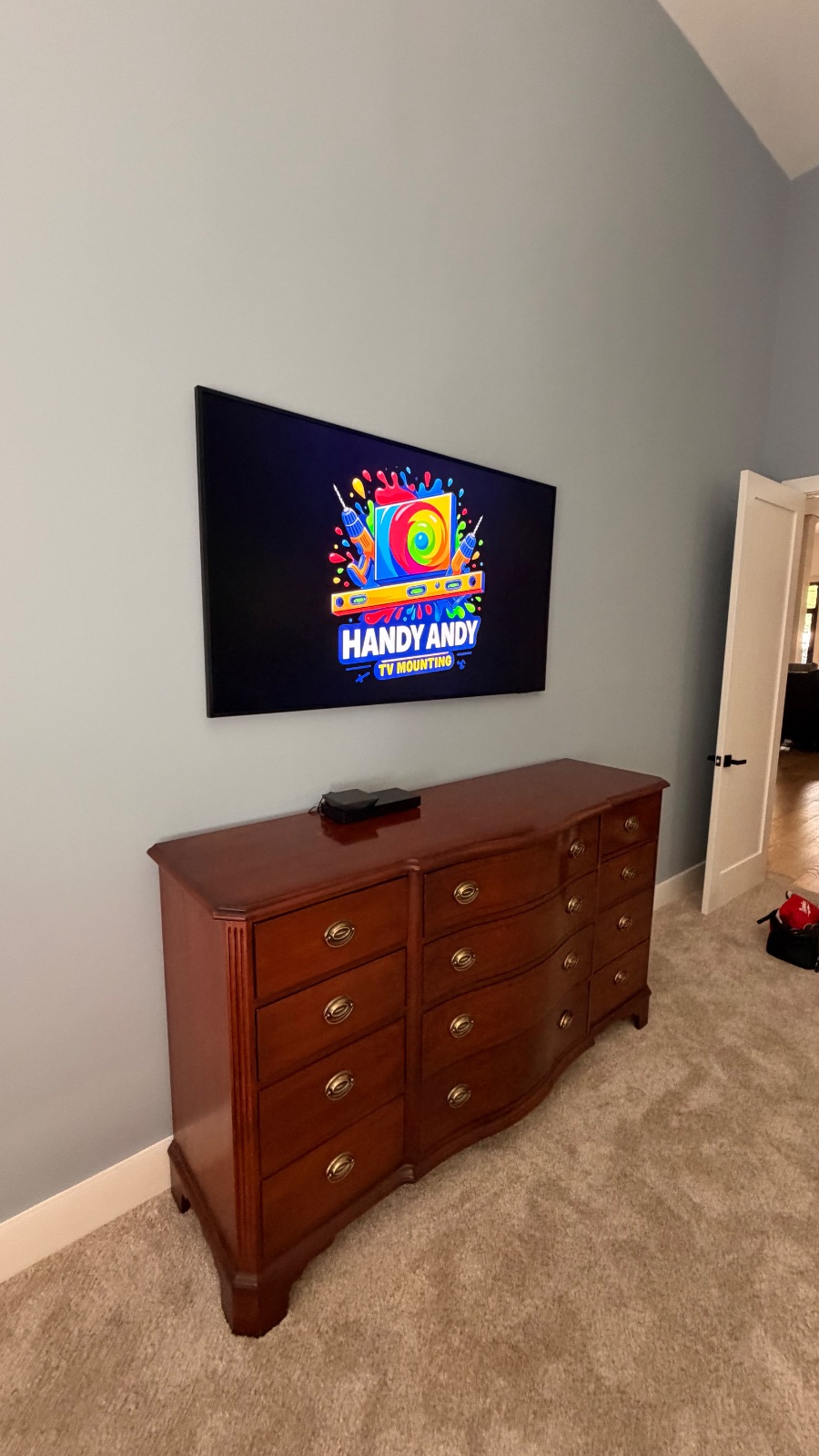 TV mounted above a wood dresser near a doorway displaying the Handy Andy logo