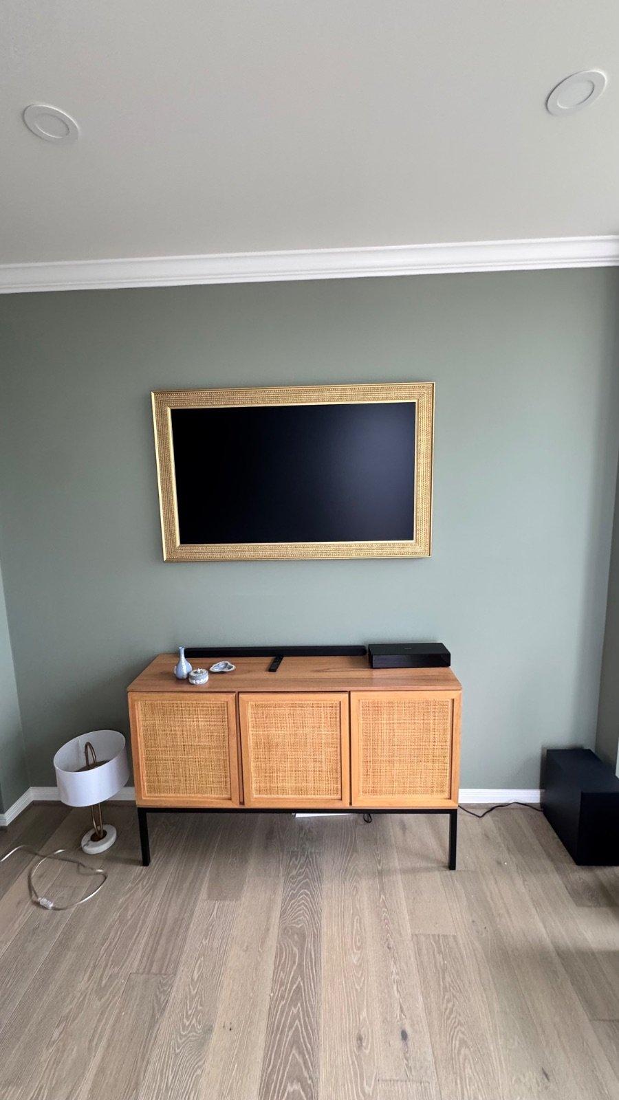 Samsung Frame TV with a custom gold art frame in off mode mounted on a sage green wall, looks like a framed painting