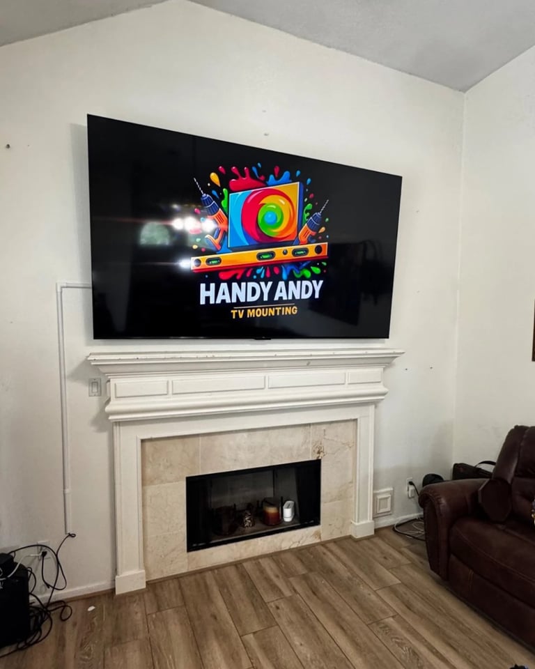 Flat-screen TV mounted above white fireplace mantel displaying Handy Andy TV Mounting logo screen