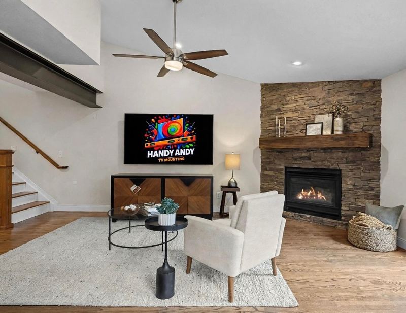 TV mounted above a wood console in a living room with a stacked-stone corner fireplace and a ceiling fan