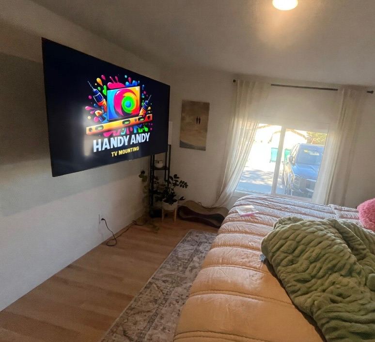 Large TV mounted on a bedroom wall across from the bed, beside a sliding glass door with sheer white curtains