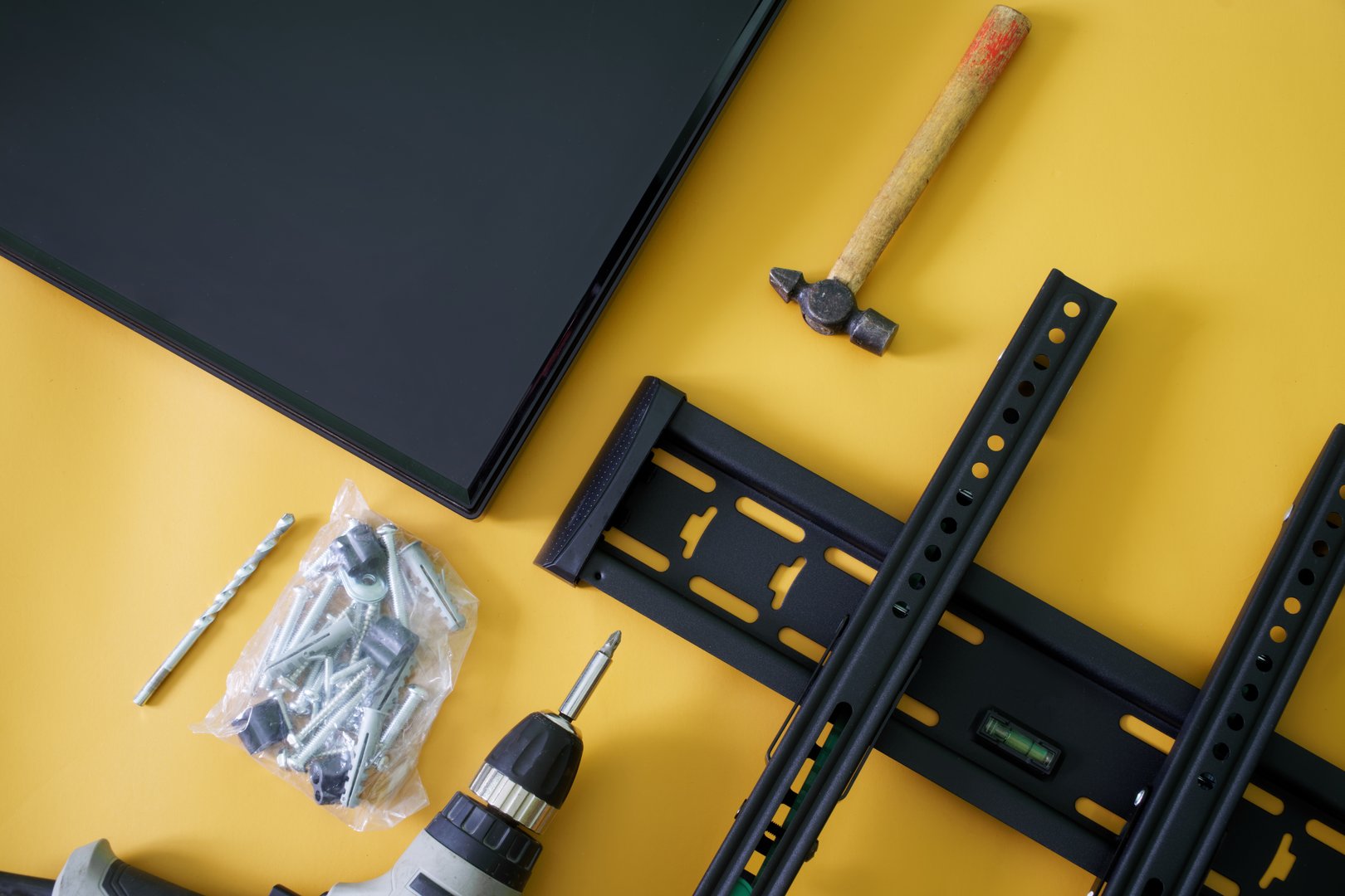 Bracket for wall mounting TV or computer monitor, an electric drill-driver, mounts and monitor screen on yellow background. Concept of wall mounting computer monitor or TV in the interior. Close-up