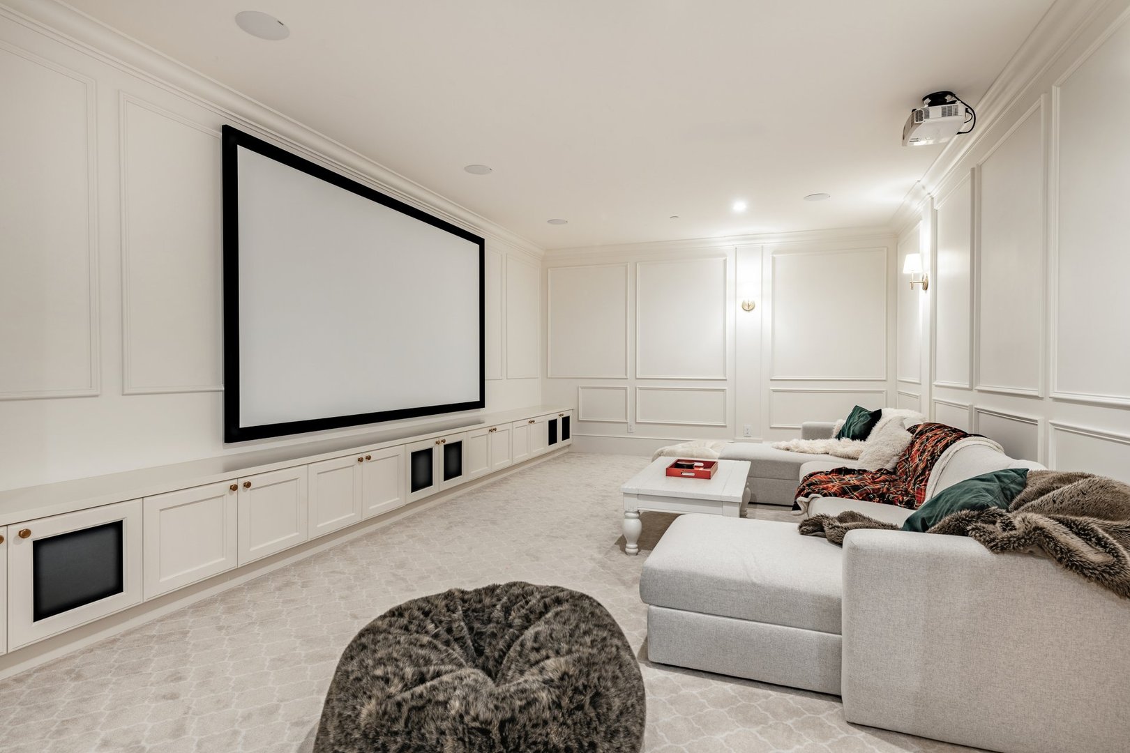 A home media theatre room with all white walls carpet sofa sectional and a very large projector and projection screen