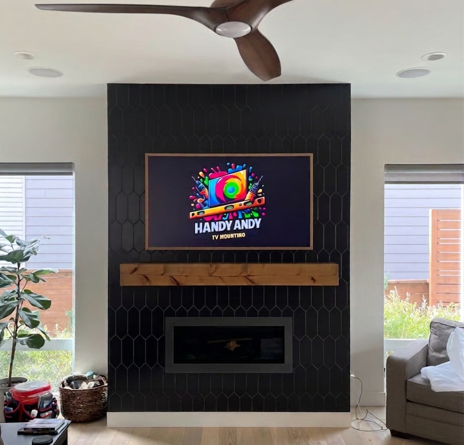 Finished Handy Andy TV mount powered on above a fireplace with a ceiling fan and windows