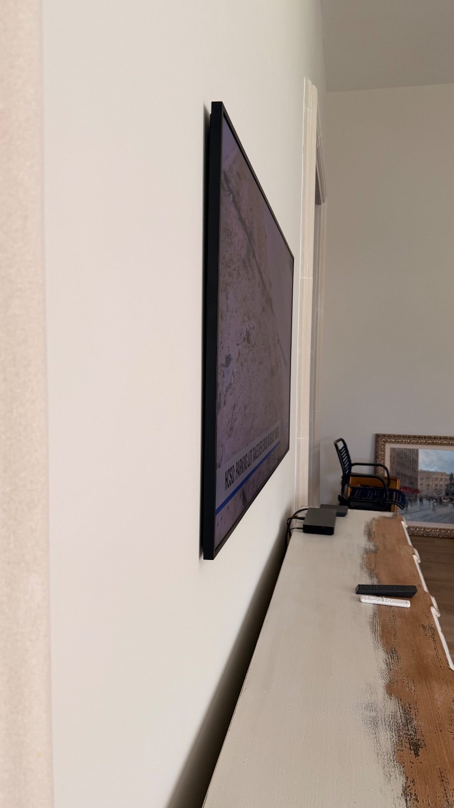 Samsung Frame TV seen edge-on against a white wall, the black frame sitting almost flat to the surface with no visible bracket gap