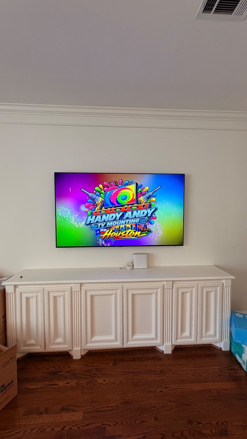 TV mounted above a long white built-in cabinet in a Houston living room, showing the Handy Andy Houston logo