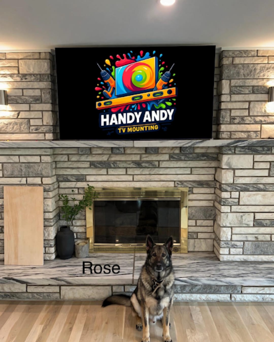 TV mounted above a stone fireplace with a German Shepherd sitting below, screen displaying the Handy Andy TV Mounting logo